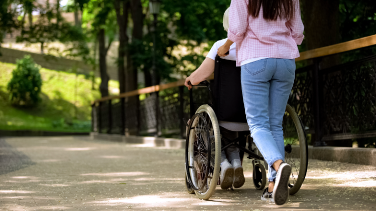 A person pushing a wheelchair, volunteering at a Aspire hospice care facility.